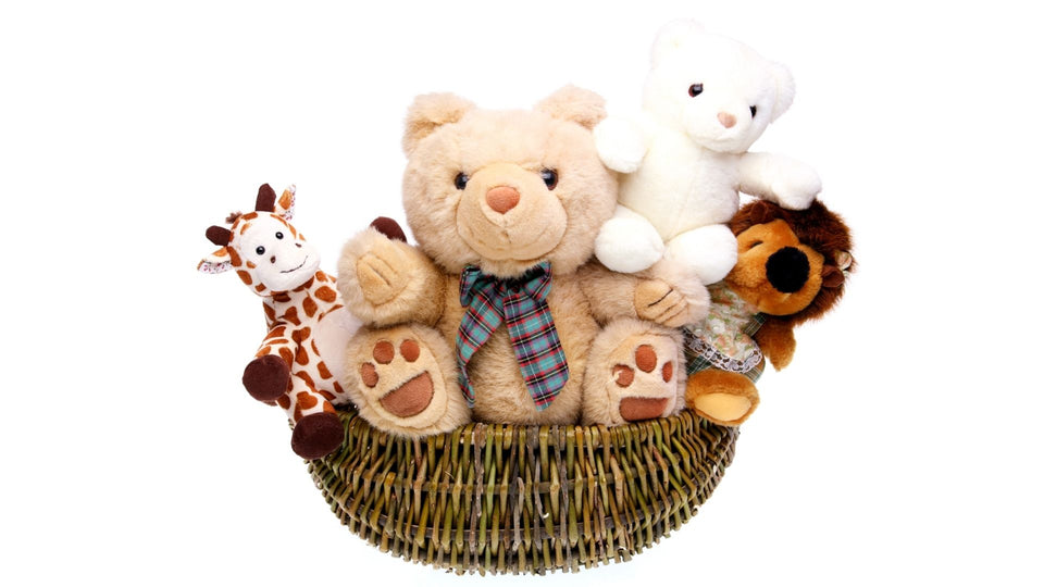 Large soft teddy bear sat in a wicker basket surrounded by other plushies including a giraffe, a white bear and a lion. 